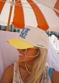 Person wearing a beige cap with blue text and yellow visor under an orange and white striped umbrella.