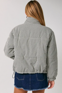 A woman shown from the back wearing a black and white gingham patterned cropped jacket and a blue denim skirt against a plain light gray studio background.