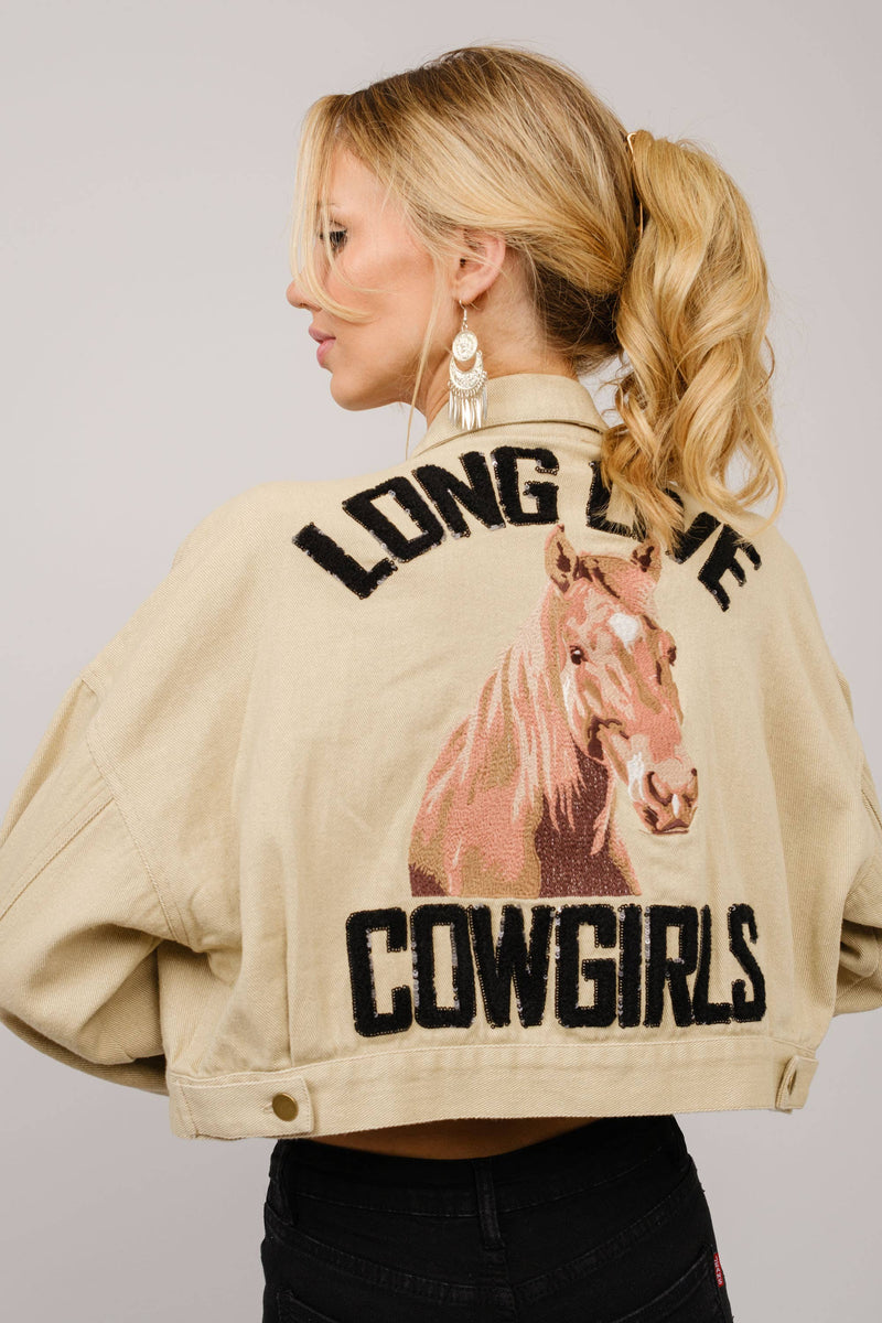 Woman wearing a beige jacket with a horse graphic and text on the back, against a plain background.