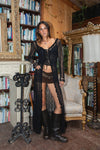 Woman in a black outfit standing in a room with bookshelves and decorative elements.