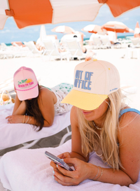 Two women on a beach with hats and umbrellas in the background