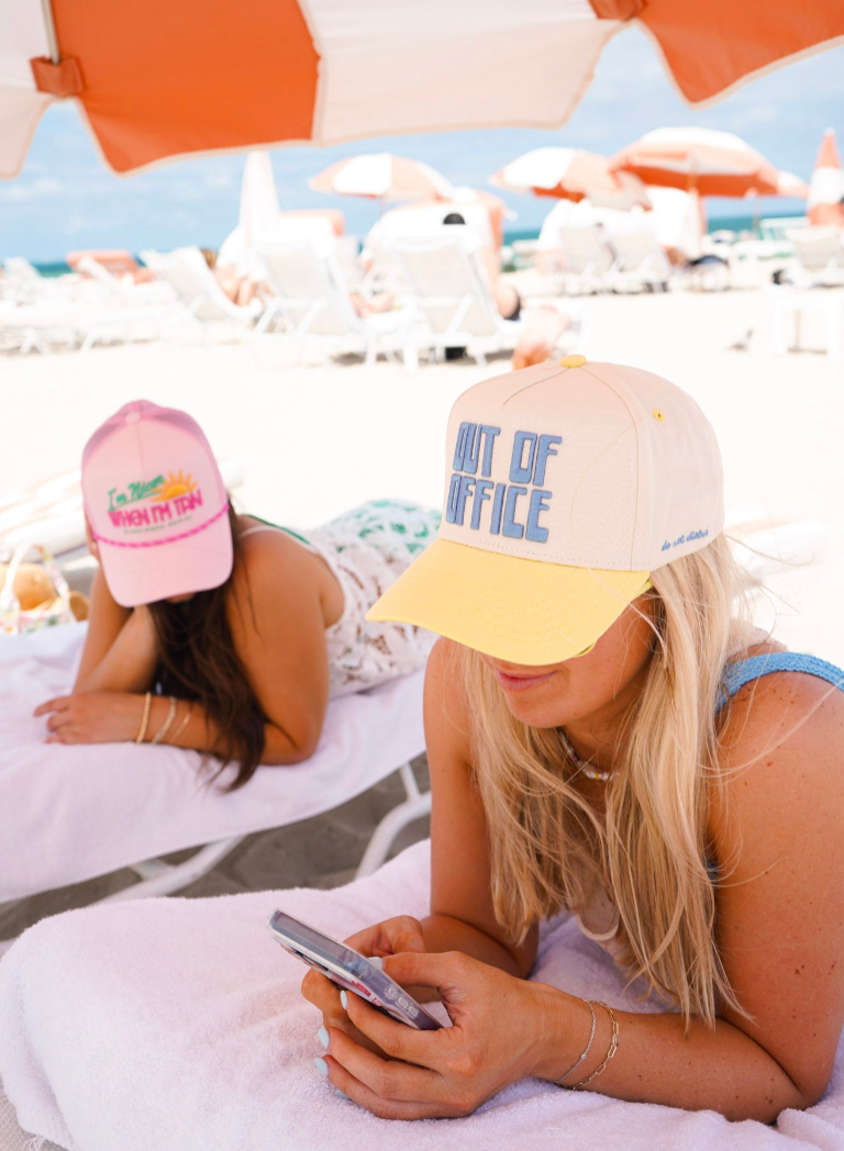 Two women on a beach with hats and umbrellas in the background