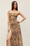 Woman wearing a strapless leopard print dress with a slit on a plain background