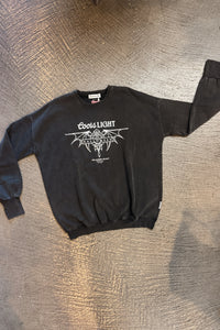 A black long-sleeve crewneck sweatshirt featuring a white graphic print of the Coors Light logo and a horned demon design, laid flat on a textured gray floor.