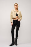 Woman wearing a beige jacket, black top, and jeans with black boots on a white background
