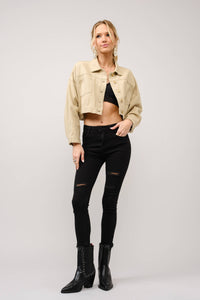 Woman wearing a beige jacket, black top, and jeans with black boots on a white background