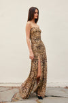 Woman wearing a leopard print strapless gown with a high slit on a plain background