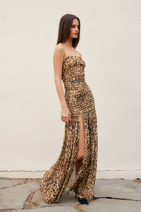 Woman wearing a leopard print strapless gown with a high slit on a plain background
