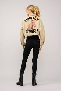Person wearing a beige jacket with text and a graphic, standing against a plain background