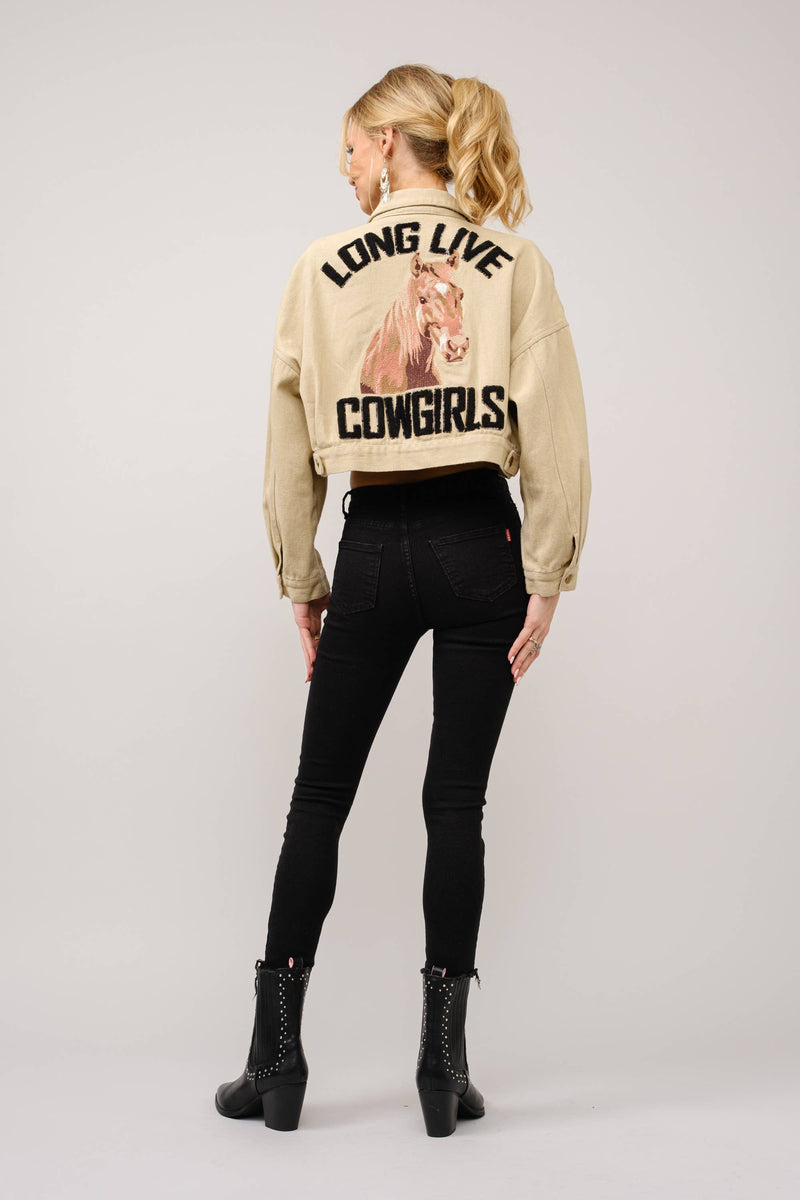 Person wearing a beige jacket with text and a graphic, standing against a plain background