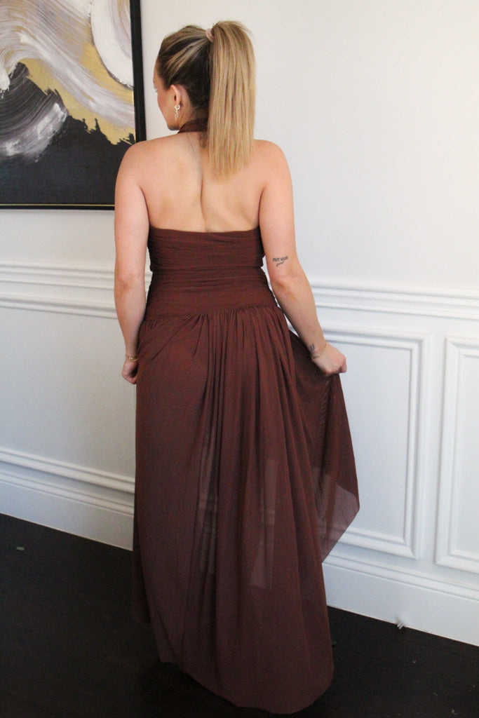 Woman wearing a brown strapless dress in a room with white walls and a framed picture.