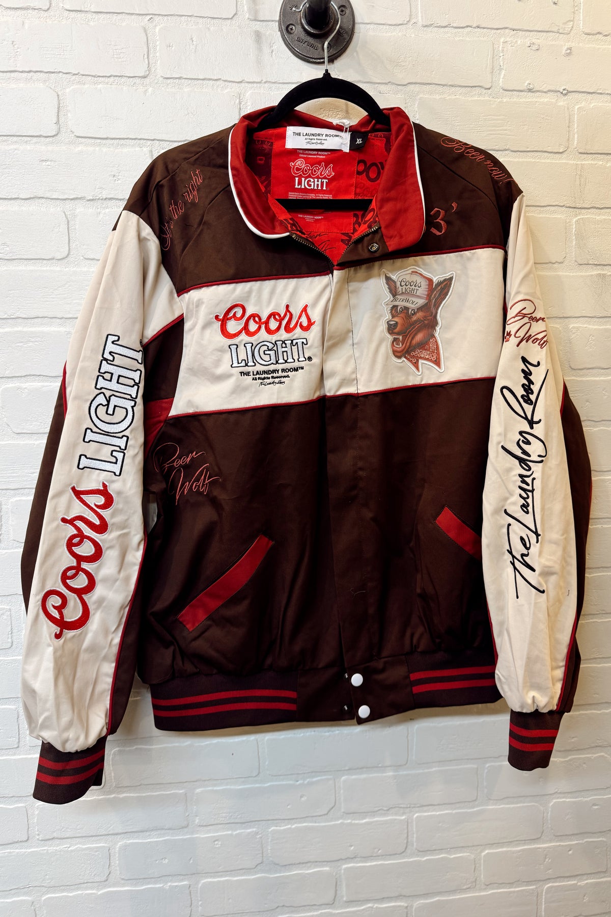 Coors Light branded jacket on a hanger against a white brick wall.