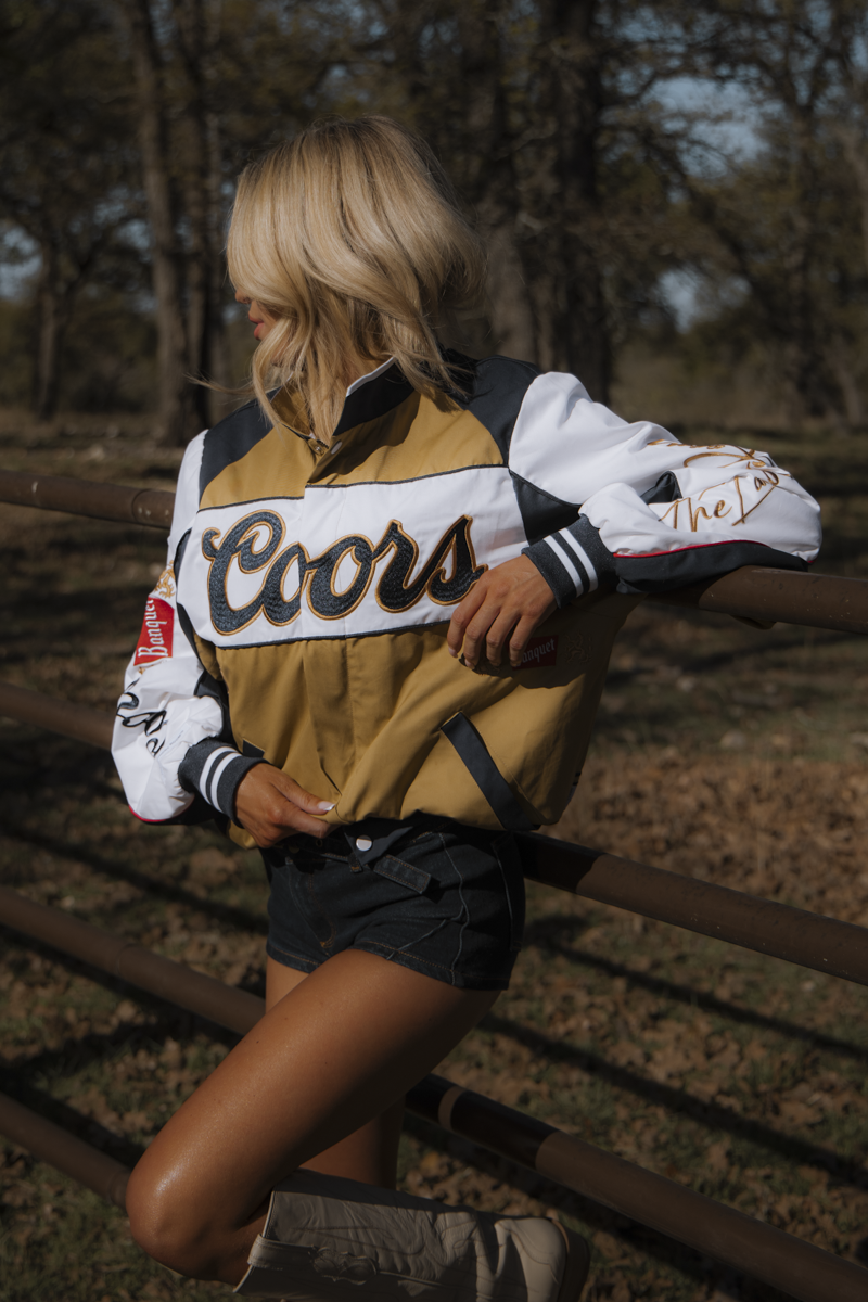 Person wearing a Coors-branded jacket standing on train tracks in a natural setting
