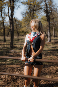 Woman standing outdoors in a wooded area, wearing a vest and shorts.