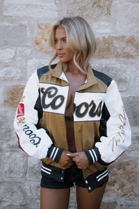 Woman wearing a varsity jacket with 'Colorado' text against a stone wall.