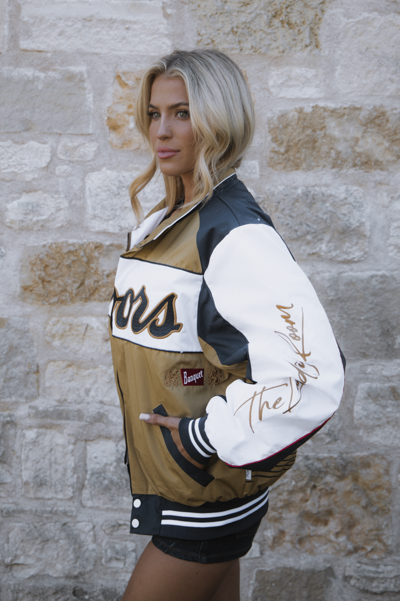 Woman wearing a varsity jacket with branding against a stone wall.