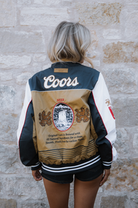 Person wearing a Coors-branded jacket against a stone wall.