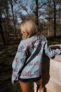 Person wearing a denim jacket with text, standing outdoors near trees.