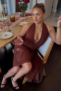 Woman in a brown dress sitting at a dining table with a glass of pink wine.