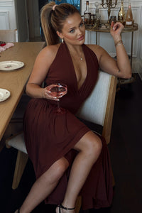 Woman in a burgundy dress holding a glass of red wine in a dining setting.