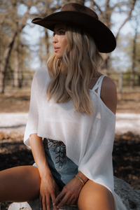 Woman wearing a white top and brown hat sitting outdoors with trees in the background