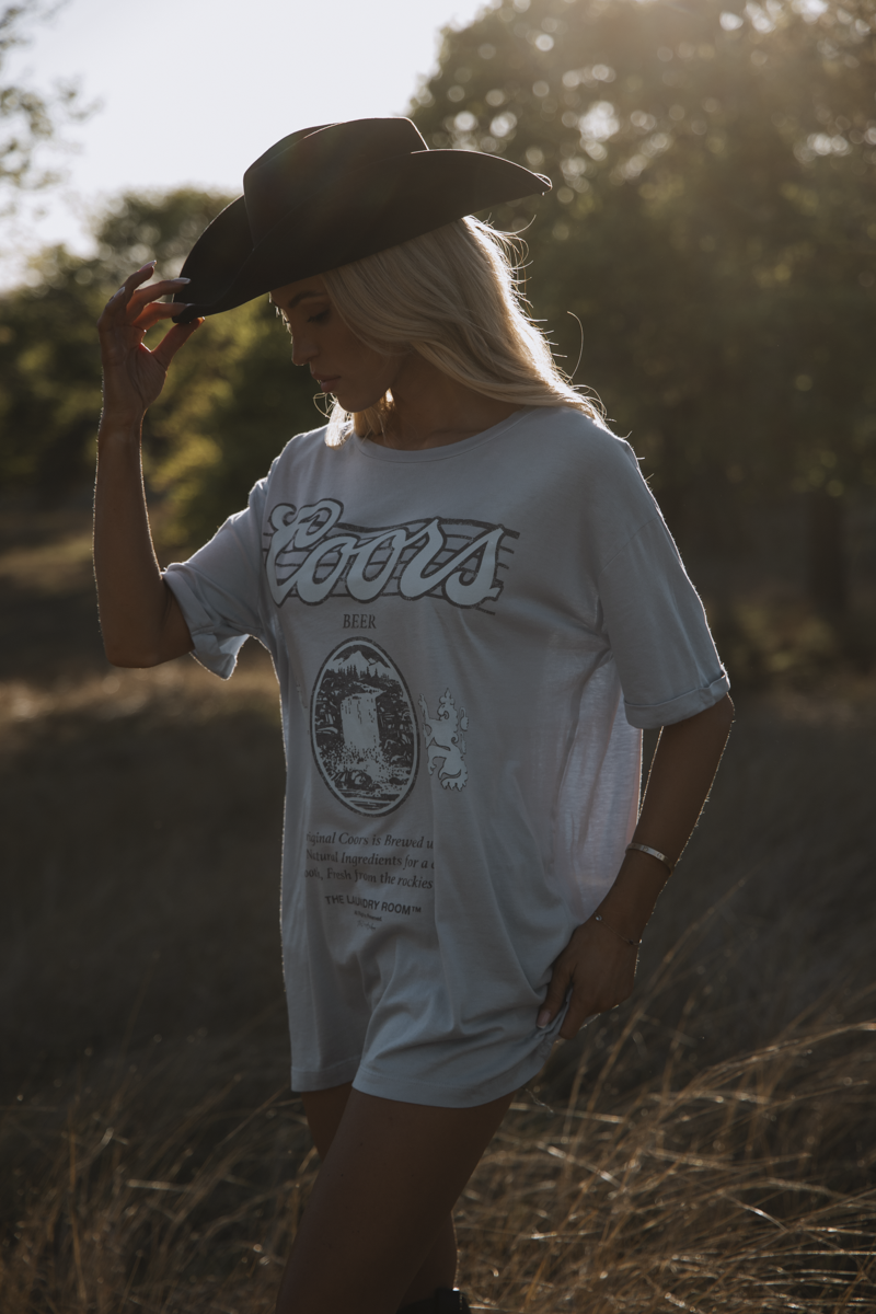 Person wearing a white t-shirt with text and graphics, standing in a natural setting.