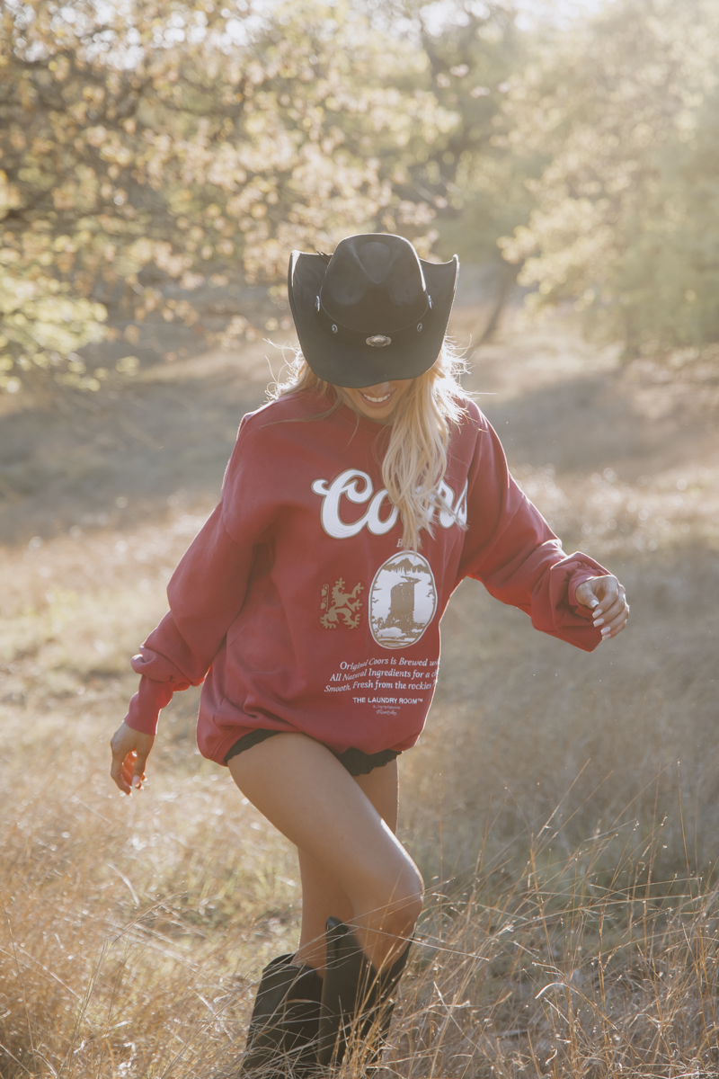 Person wearing a red sweatshirt with a logo and text, standing in a natural setting.