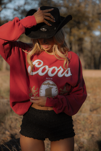 Person wearing a red Coors sweatshirt and black cowboy hat in an outdoor setting