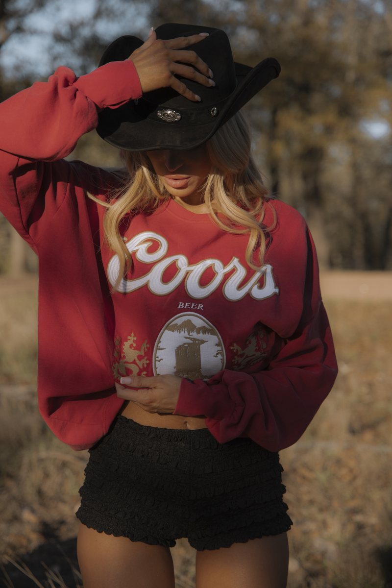 Person wearing a red Coors sweatshirt and black cowboy hat in an outdoor setting