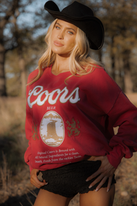 Person wearing a red Coors Beer sweatshirt outdoors with trees in the background