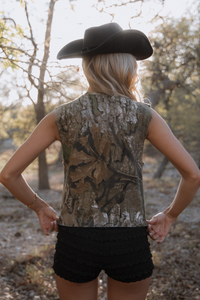 Person wearing a camouflage sleeveless shirt and black cowboy hat in a natural setting.