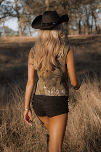 Woman in a cowboy hat and patterned top walking through a field.