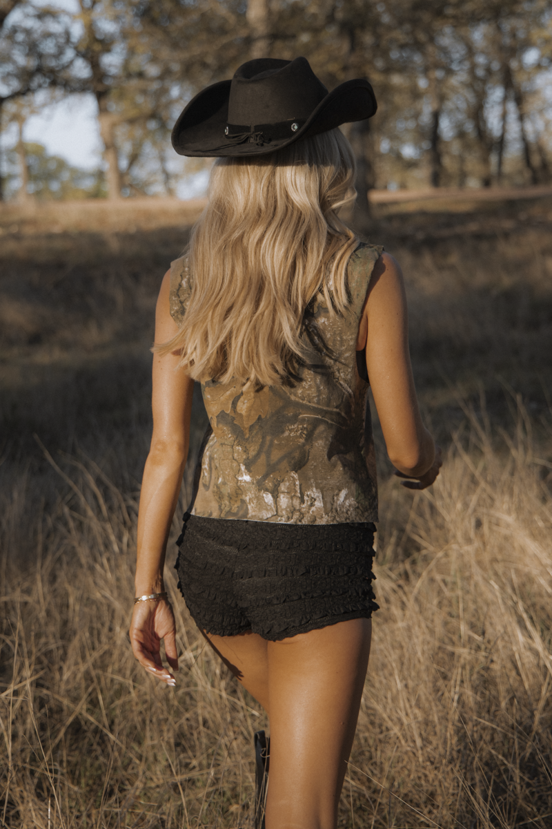 Woman in a cowboy hat and patterned top walking through a field.