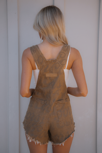 Person wearing brown denim overalls against a plain background