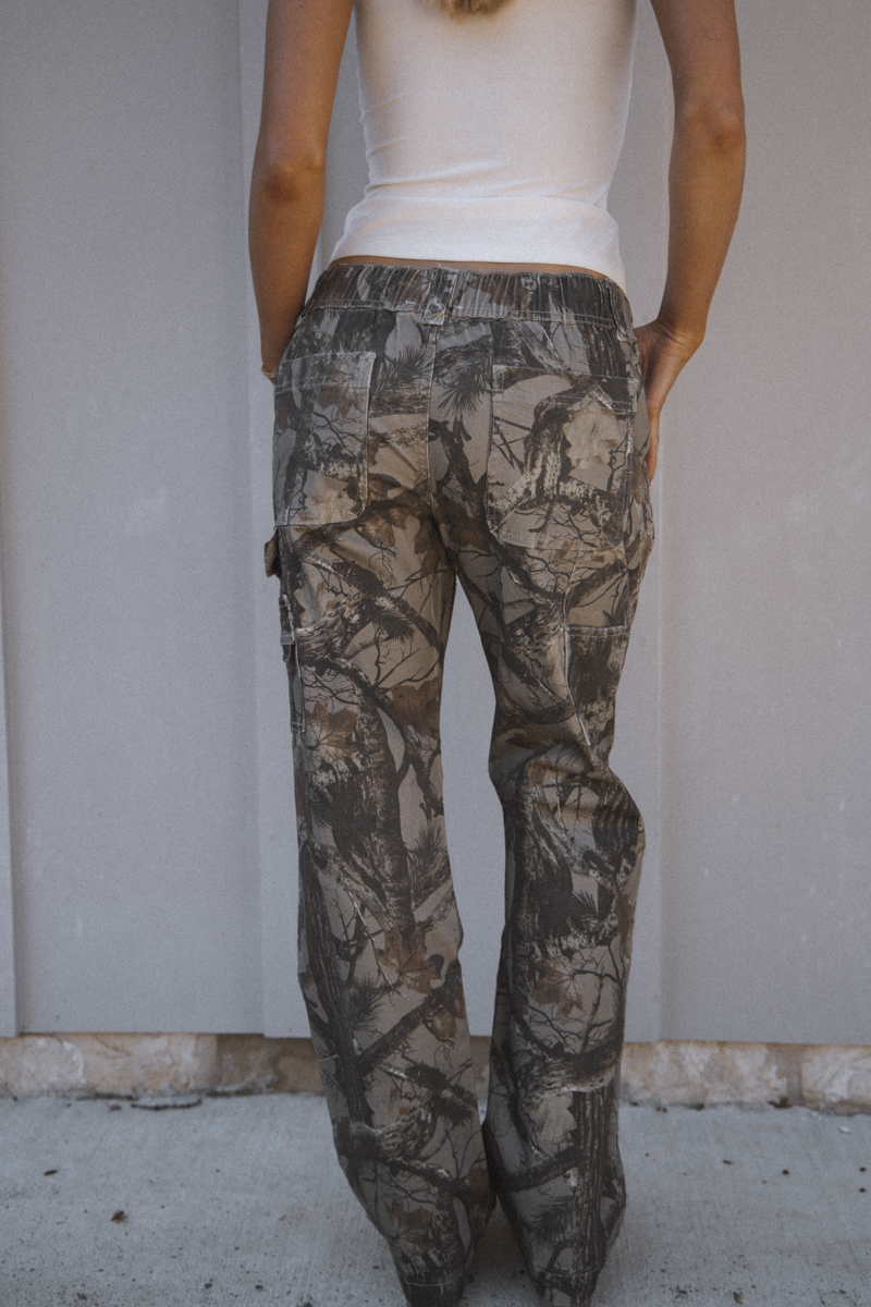 Person wearing camouflage pants against a plain background