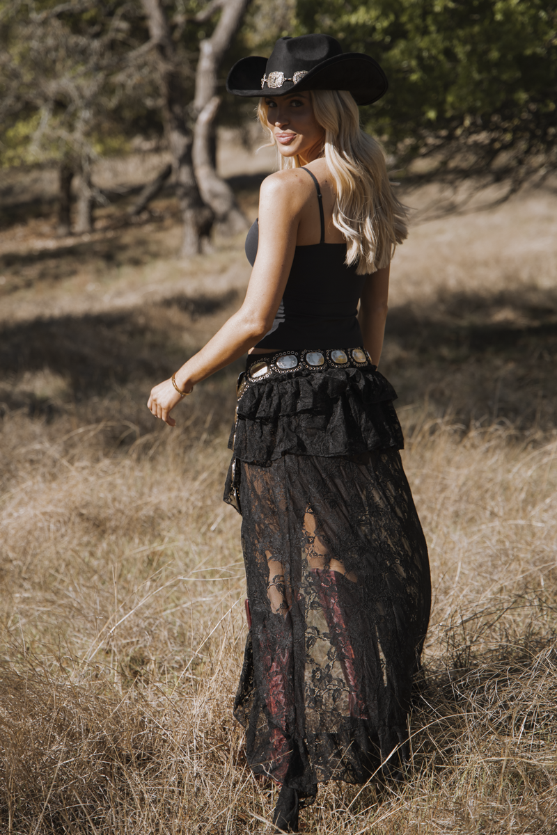 Woman in a black outfit with a cowboy hat standing in a natural setting