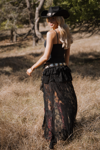Woman in a black outfit with a cowboy hat standing in a natural setting