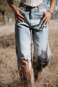 Person wearing light blue jeans standing in a field with trees in the background
