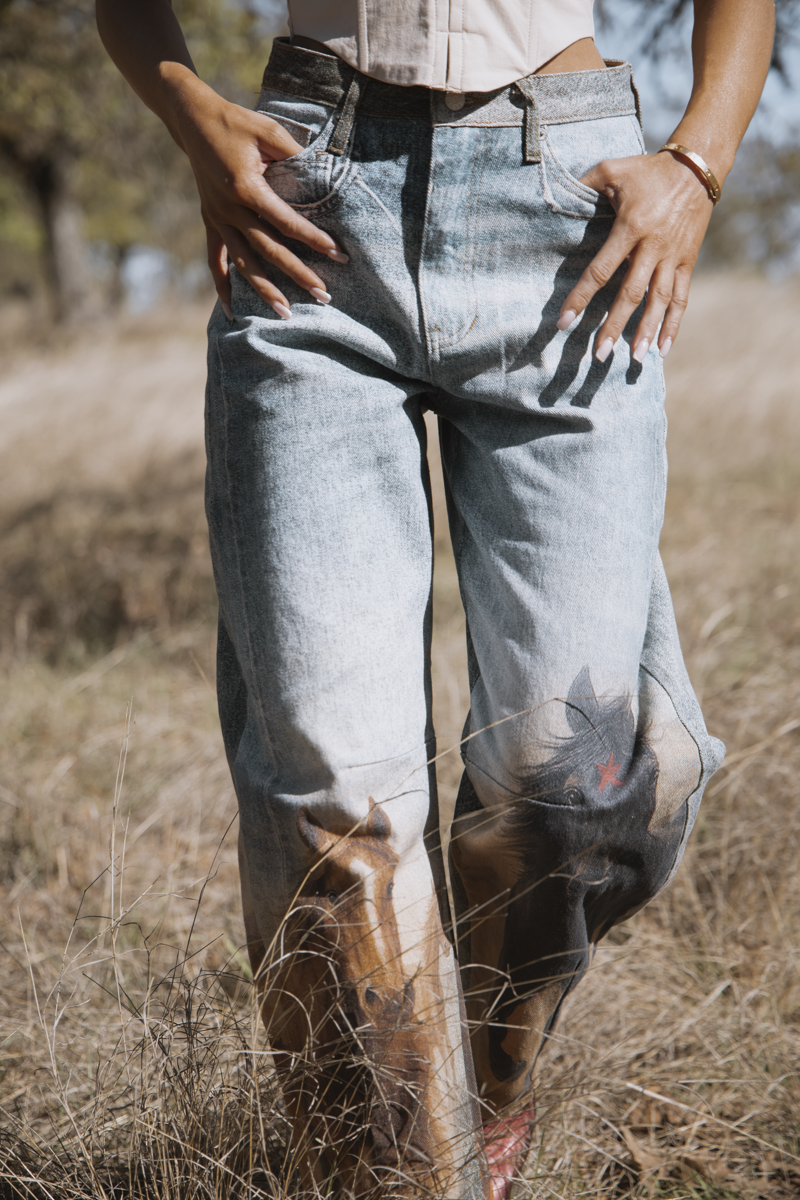 Person wearing light blue jeans standing in a field with trees in the background