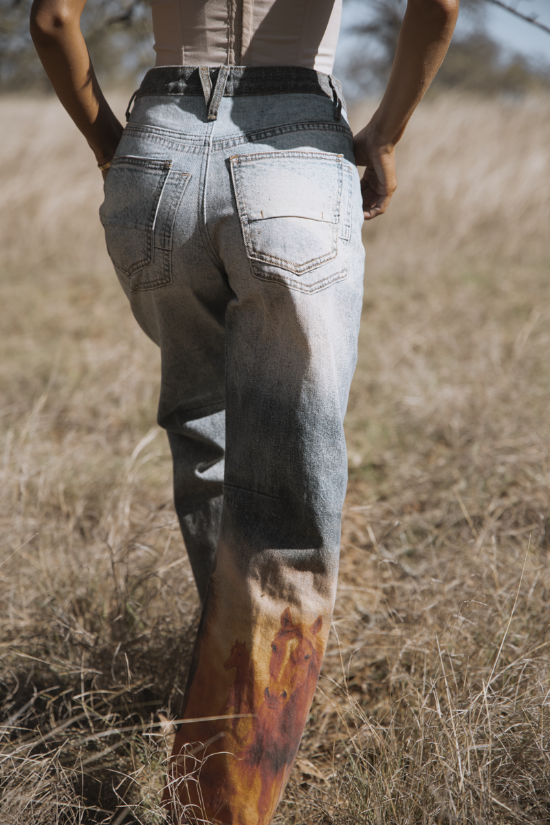 Person wearing distressed jeans standing in a field with a focus on the pants.