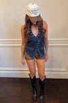 Woman wearing a denim vest, shorts, and cowboy boots with a cap indoors.