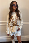 Woman wearing a cream-colored sweater with lace details and white shorts against a neutral background