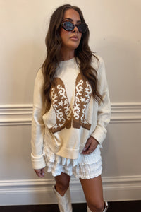 Woman wearing a cream-colored sweater with lace details and white shorts against a neutral background