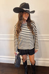 Woman wearing a striped sweater, black skirt, and cowboy hat against a white wall.
