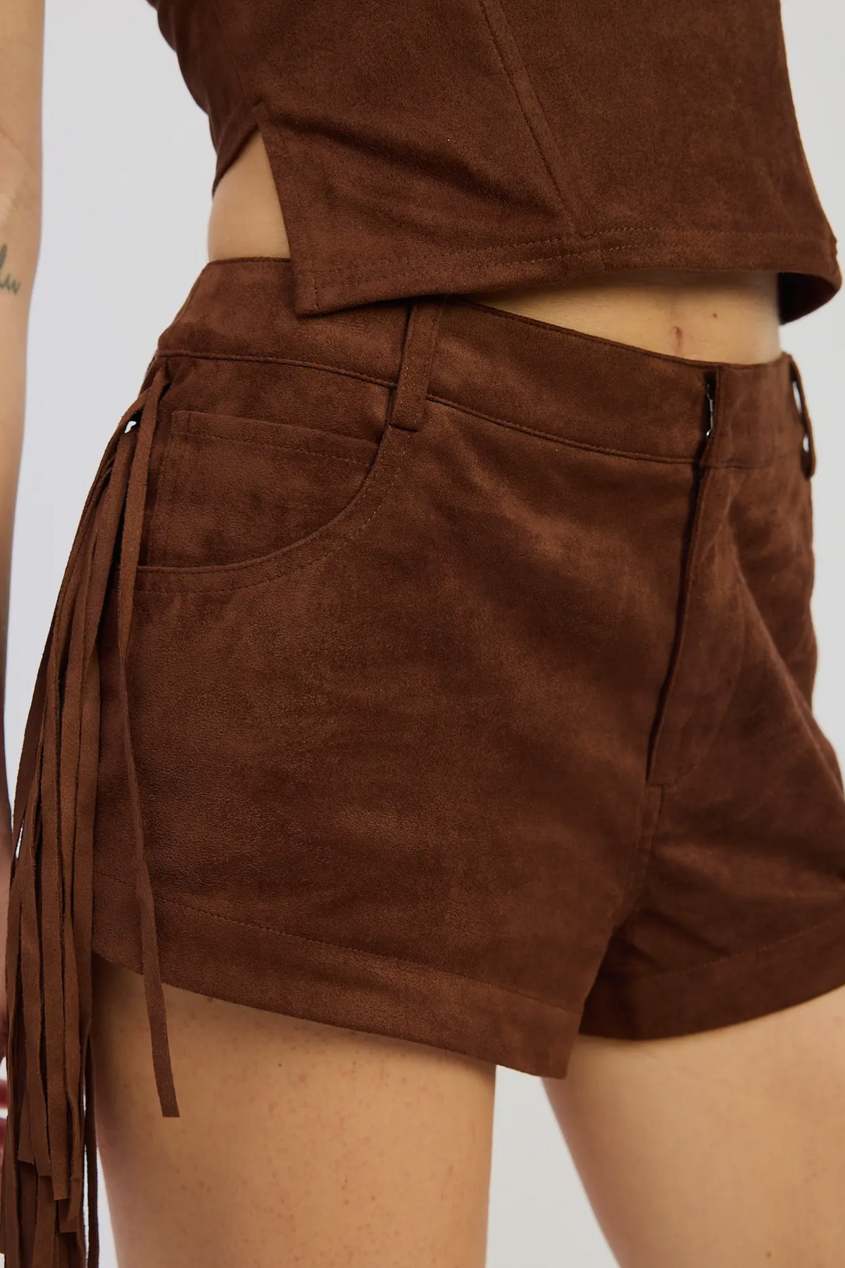 Brown suede shorts with fringe details on a plain background