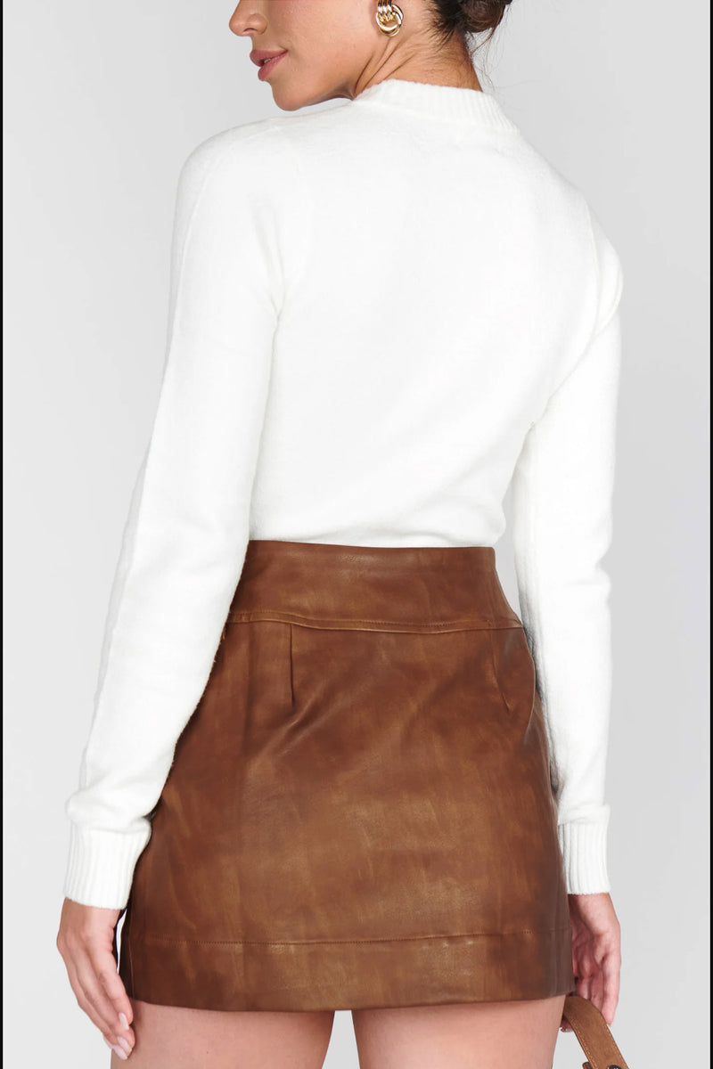 Person wearing a white long-sleeve top and brown leather skirt on a plain background