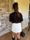 Woman in black top and white shorts standing on a wooden deck.