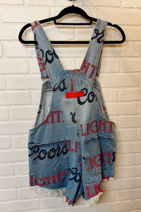Denim overalls with text pattern on a hanger against a brick wall.