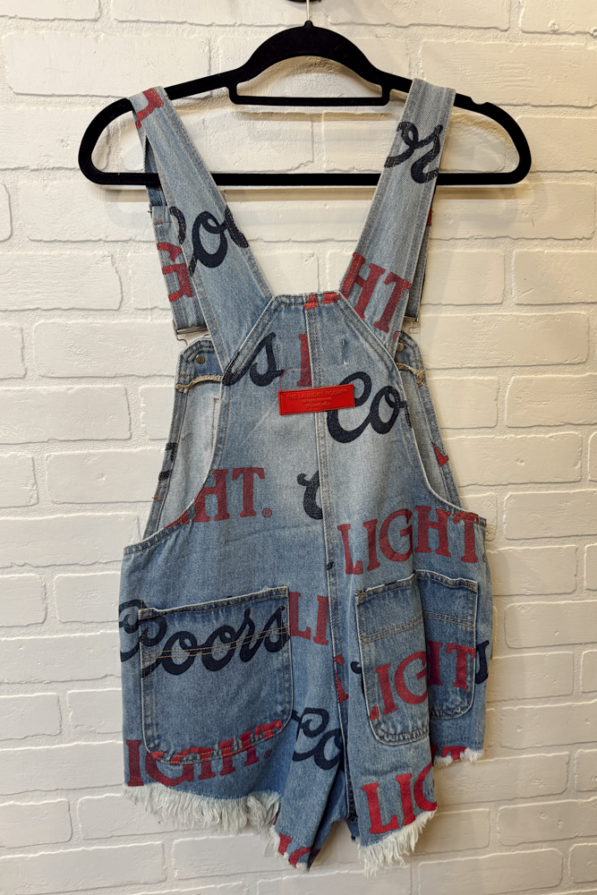 Denim overalls with text pattern on a hanger against a brick wall.