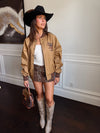 Woman in a stylish outfit with a cowboy hat, jacket, and boots indoors.